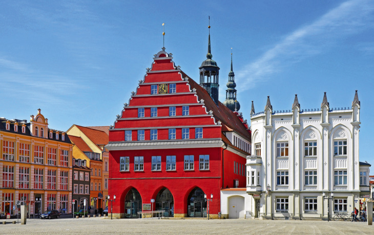 Historische Gebäude an einem Marktplatz unter blauem Himmel.