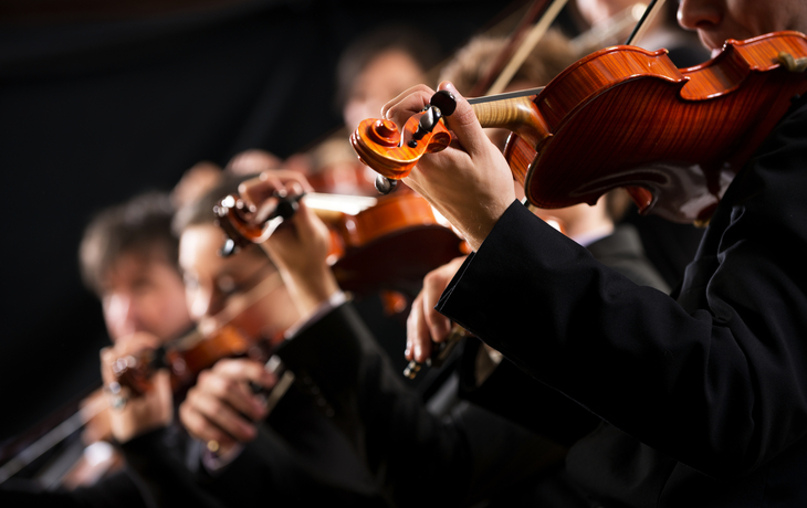Nahaufnahme von Geigenspielern in einem Orchester.