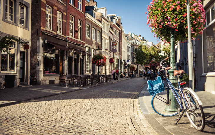 Maastrichter Straßen mit Kopfsteinpflaster, Fahrrad und Blumen im Sommer.