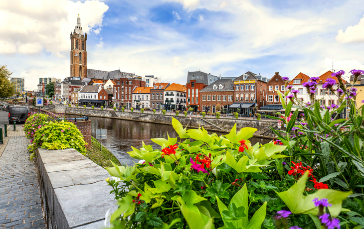 Blumen im Vordergrund, Kanal mit Brücke und Kirchturm im Hintergrund.