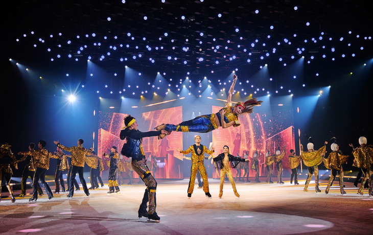 Eiskunstläufer in bunten Kostümen bei einer Bühnenshow mit Lichteffekten.