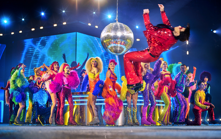 Bunte Tanzgruppe auf der Bühne mit Discokugel oben.