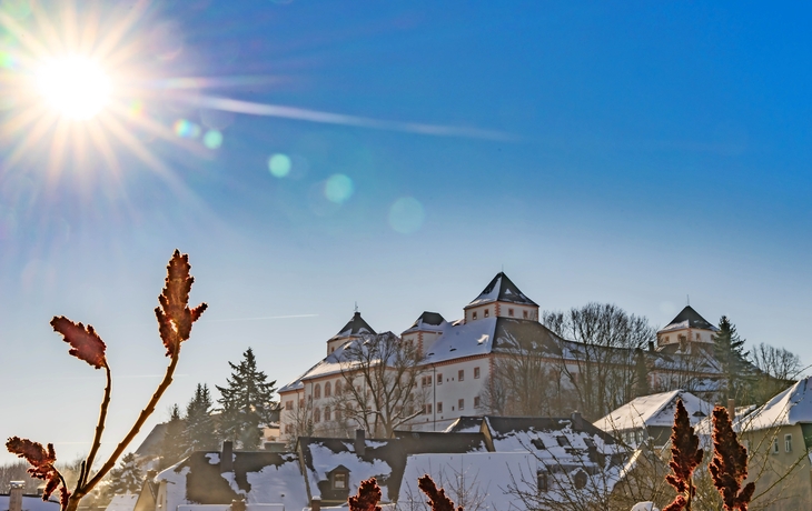 Winterlandschaft mit Schloss und Sonne am blauen Himmel.