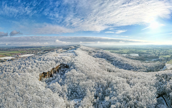 Schneebedeckte Landschaft mit bewaldeten Hügeln unter blauem Himmel.