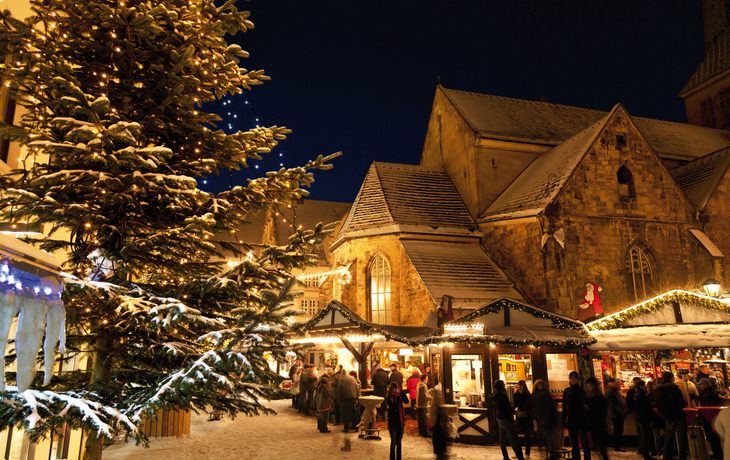 Weihnachtsmarkt in Hameln bei Nacht mit beleuchtetem Tannenbaum und Ständen.