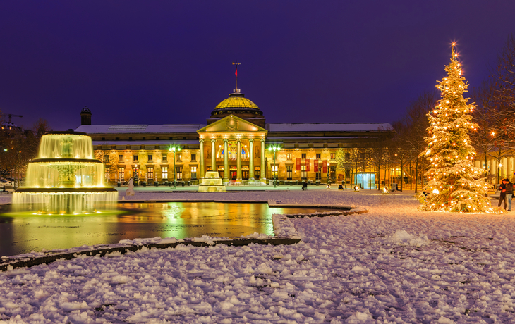 Schneebedecktes Kurhaus in Wiesbaden bei Nacht mit beleuchtetem Weihnachtsbaum.