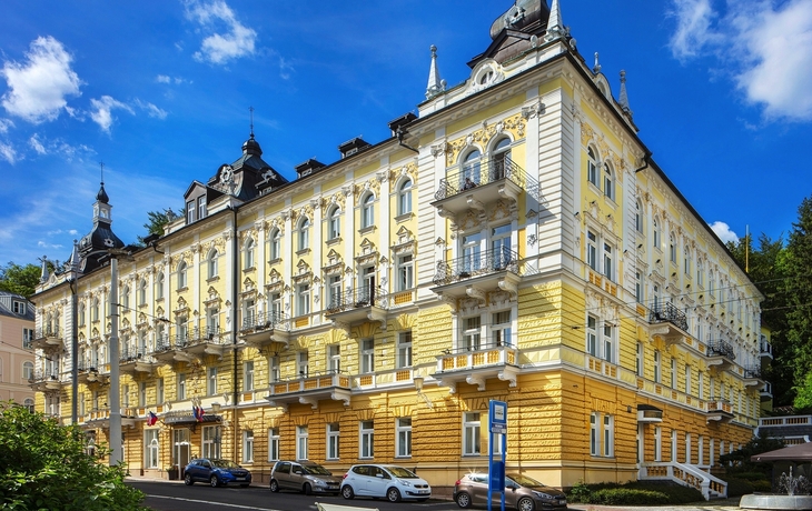 Historisches Gebäude in Marienbad mit gelber Fassade unter blauem Himmel.