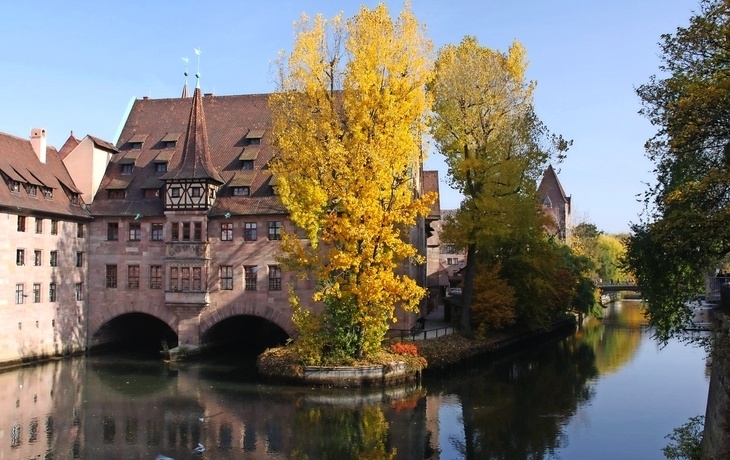 Historisches Gebäude mit Herbstbäumen an einem Fluss.