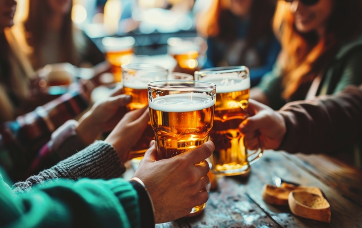 Gruppe von Freunden stößt mit Biergläsern an einem rustikalen Holztisch in einer Brauerei an.