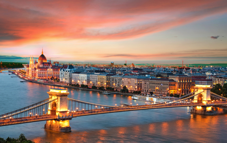 Panoramablick auf Budapest mit Kettenbrücke und Parlamentsgebäude bei Sonnenuntergang.
