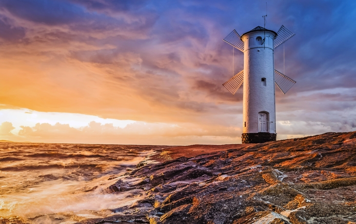 Ein Leuchtturm auf einem Felsen am Meer bei Sonnenuntergang.