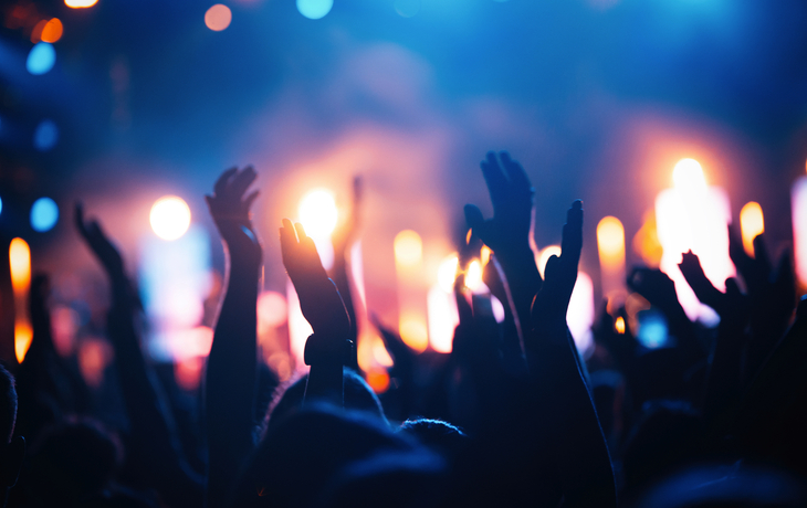 Personen heben Hände bei einem Konzert mit bunten Lichtern im Hintergrund.