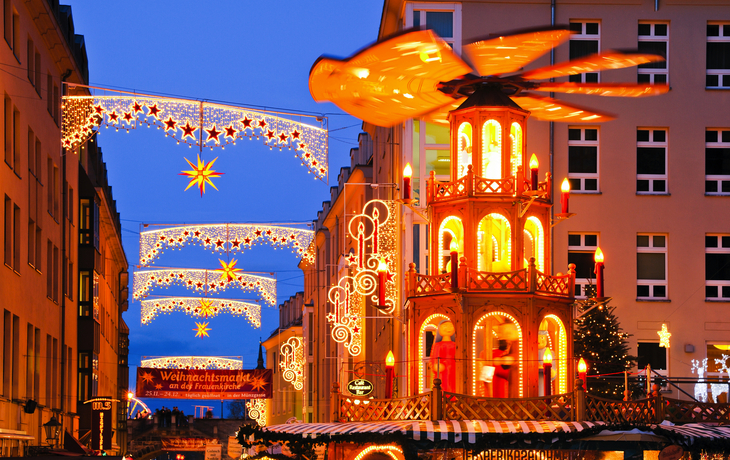 Weihnachtsmarkt mit beleuchteter Pyramide und Sternendekorationen bei Nacht.
