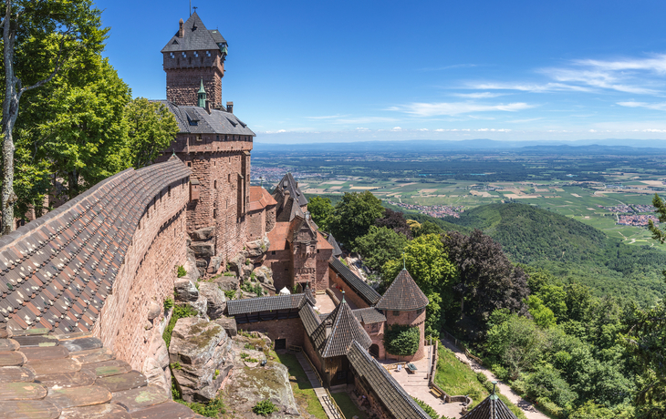 Burg mit Türmen und Mauern, umgeben von üppiger Landschaft und Blick in die Ferne