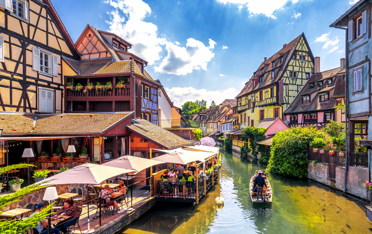 Fachwerkhäuser an einem Kanal mit Boot und Touristen in einer malerischen Altstadt.