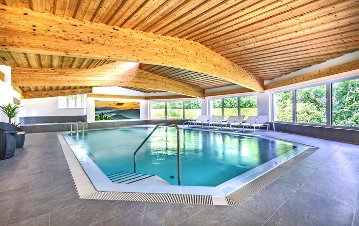 Indoor-Pool mit Holzdecke und Liegen im Forellenhof Flachau.
