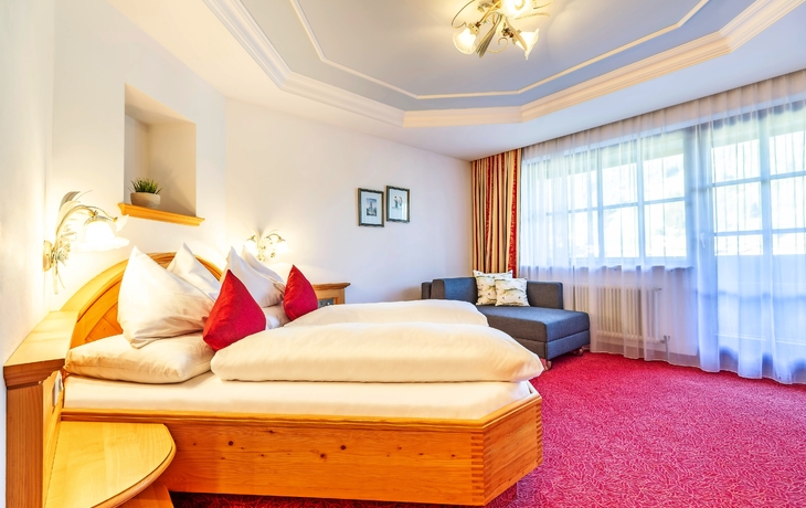 Helles Zimmer mit Doppelbett, rotem Teppich und Sofa im Forellenhof Flachau.