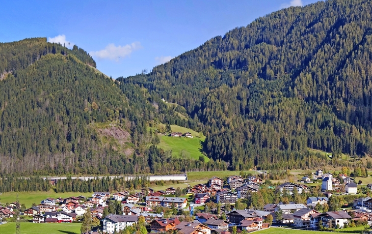 Dorf Flachau im Sommer, umgeben von Wiesen und Wäldern in den österreichischen Alpen.
