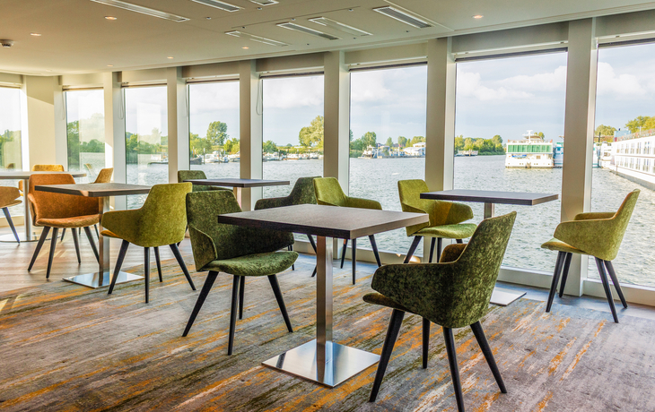 Sitzbereich in Lounge mit Tischen und Stühlen, Fenster mit Blick auf Wasser.