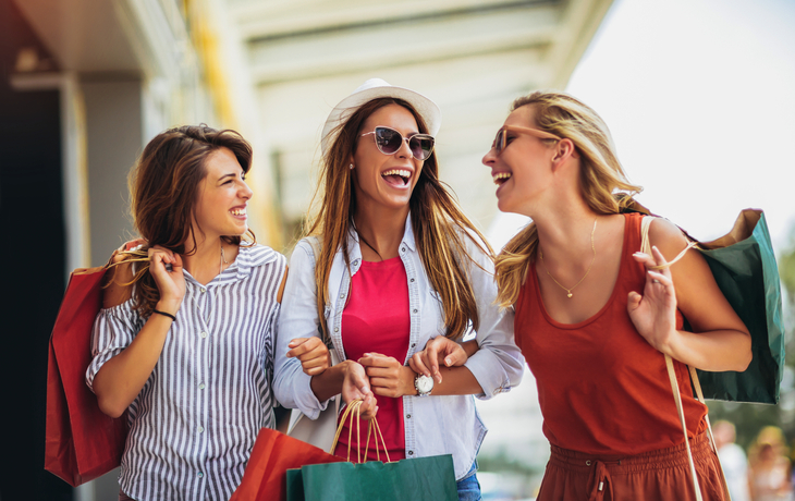 Drei lachende Frauen mit Einkaufstaschen beim Einkaufsbummel in der Stadt.