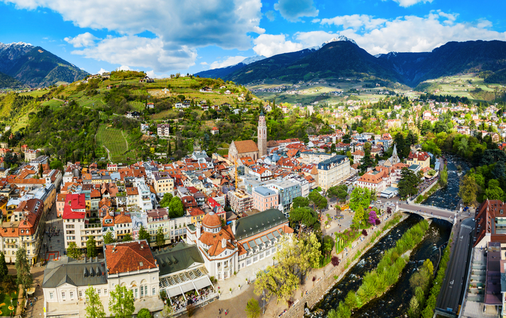 Blick auf eine malerische Stadt inmitten von Bergen mit Fluss und historischen Gebäuden.