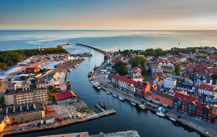 Luftaufnahme eines Hafens mit Gebäuden und einer Flussmündung in die Ostsee.