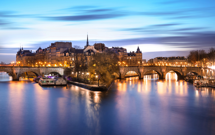 Île Saint-Louis in Paris bei Dämmerung, beleuchtet, mit der Seine im Vordergrund.