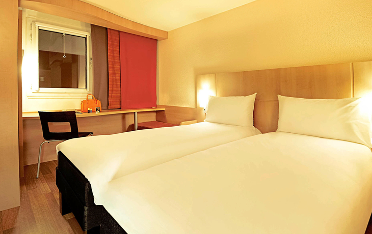 Helles Hotelzimmer mit zwei Einzelbetten, Schreibtisch und Fenster.