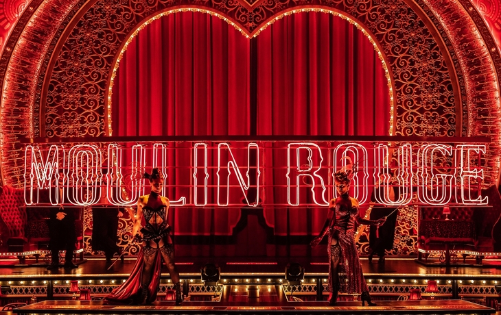 Bühne mit leuchtendem Moulin Rouge-Schriftzug und Darstellern in roten Kostümen.