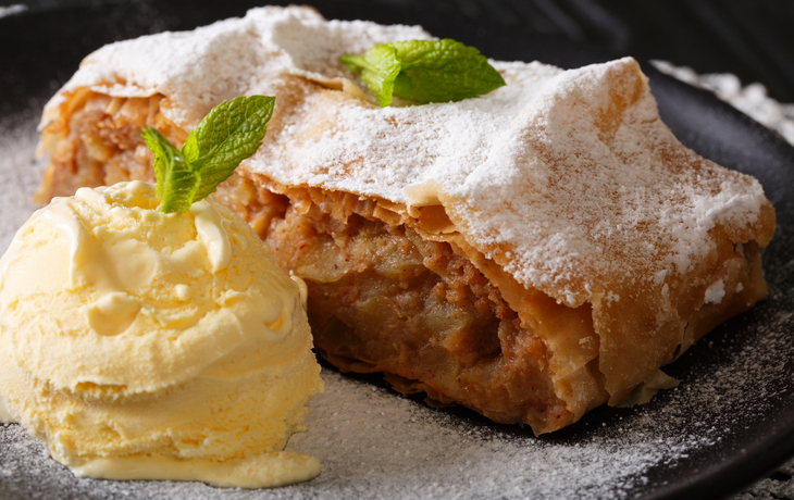 Österreichischer Apfelstrudel mit Vanilleeis, Puderzucker, Minze auf einem Teller.