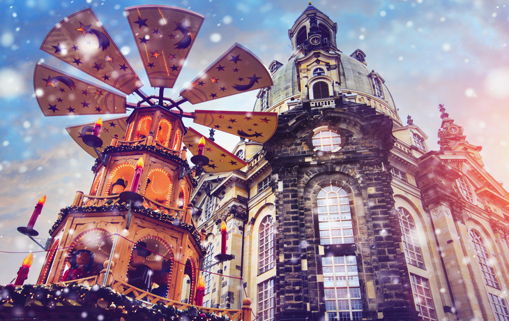 Weihnachtspyramide vor historischer Kirche mit Schneefall im Hintergrund.