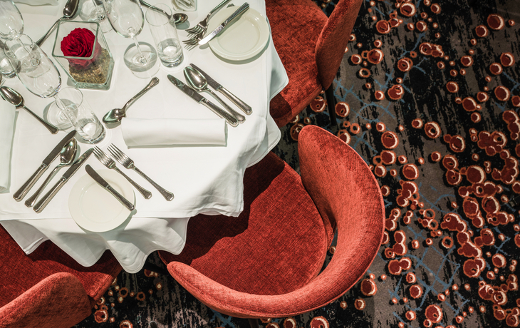 Gedeckter Tisch mit weißen Tischdecken und roten Stühlen in elegantem Restaurant.