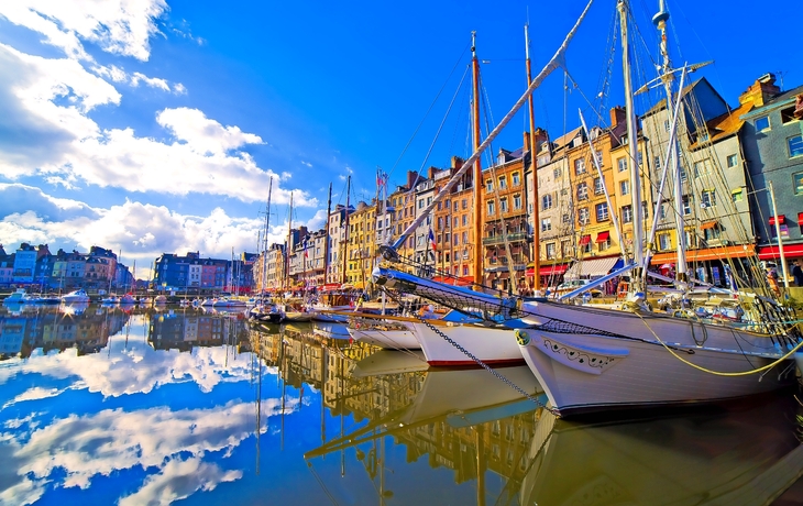 Boote in einem Hafen vor bunten Gebäuden und blauem Himmel.