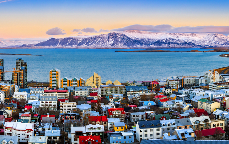 Panorama von Reykjavík mit bunten Häusern und schneebedeckten Bergen im Hintergrund.
