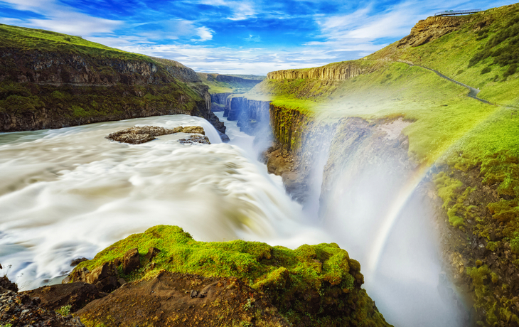 Wasserfall in einer grünen Schlucht mit Regenbogen und blauem Himmel