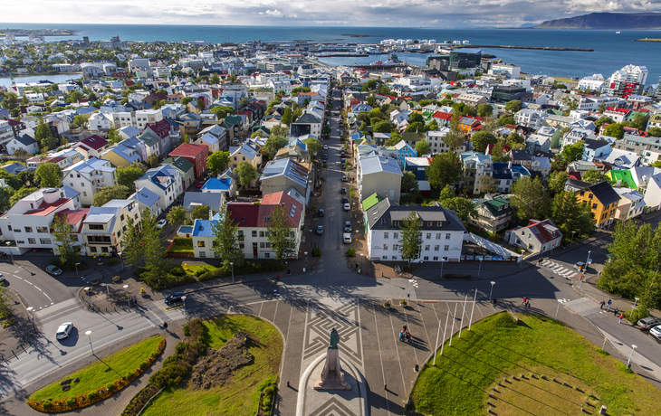 Blick auf die Küstenstadt Reykjavík mit bunten Häusern, Straßen und einem Hafen im Hintergrund.