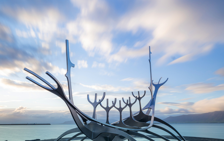 Skulptur eines stilisierten Wikingerboots am Meer unter blauem Himmel.