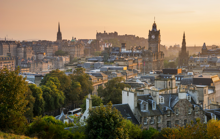 Stadtansicht von Edinburgh bei Sonnenuntergang mit historischen Gebäuden und grünem Vordergrund.
