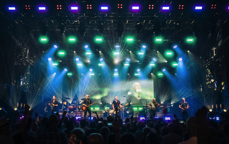 Konzertfoto von Band mit buntem Licht auf großer Bühne.