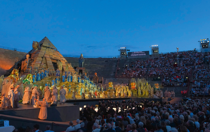 Bühnenaufführung von Verdis Aida in antikem Stadion mit Pyramide und Publikum.