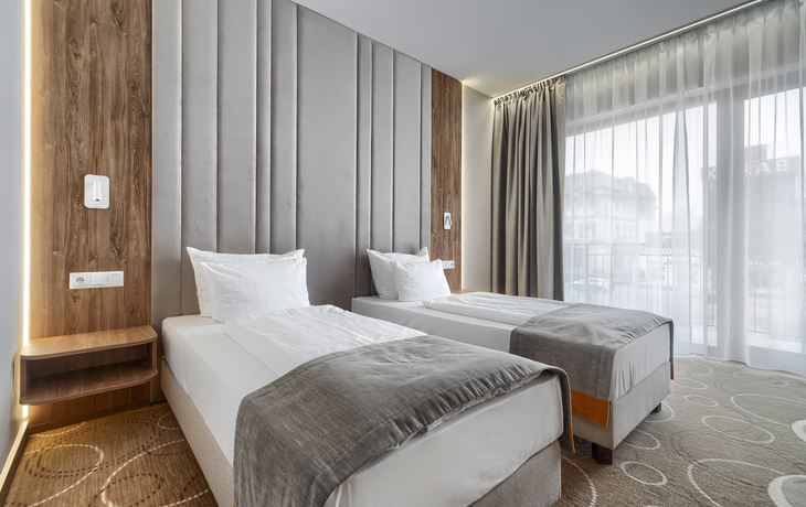 Modernes Hotelzimmer mit zwei Einzelbetten und großen Fenstern.