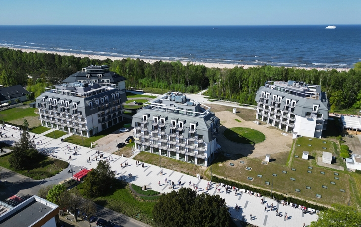 Hotelgebäude am Meer mit grüner Umgebung und Strand im Hintergrund