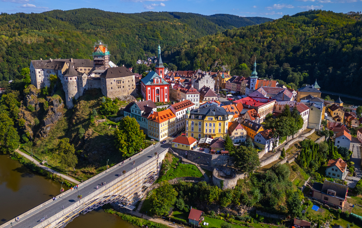 Luftaufnahme einer historischen Burg und Stadt auf einem Hügel mit Fluss und Brücke.