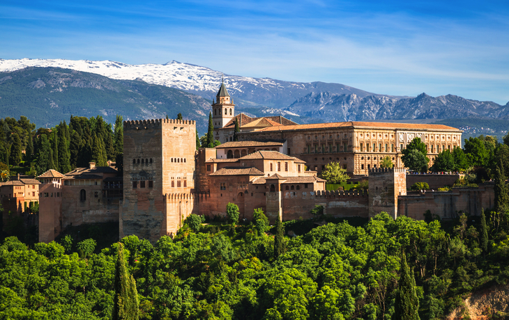 Die Alhambra in Granada vor verschneiten Bergen und blauem Himmel.