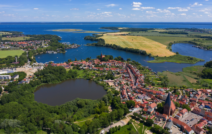 Luftaufnahme einer Stadtlandschaft mit Seen und Feldern im Hintergrund.