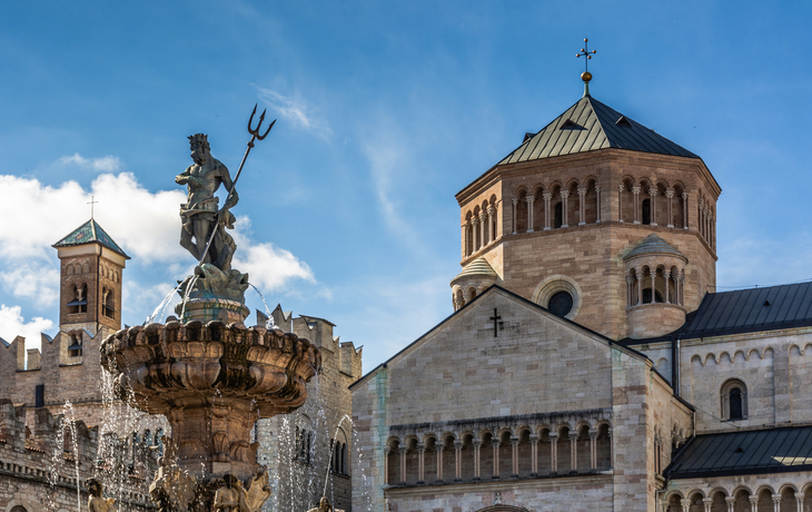 Brunnen mit Neptunstatue vor einem historischen Gebäude bei blauem Himmel.