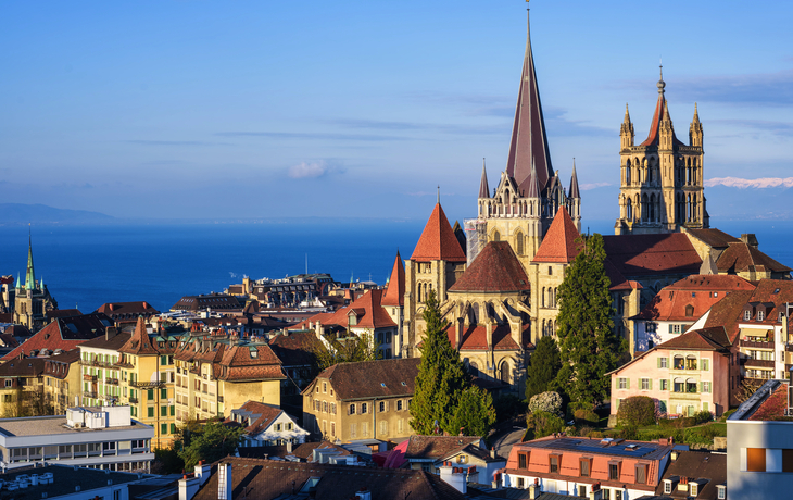 Stadtpanorama mit gotischer Kathedrale und Sicht auf den Genfersee bei klarem Wetter.