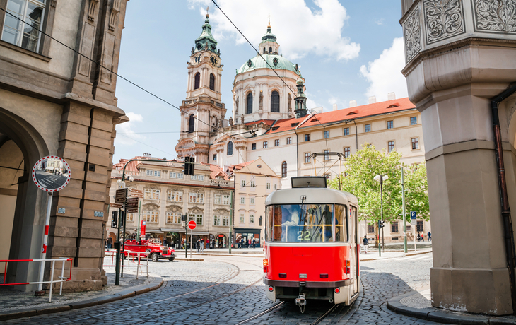 Rote Straßenbahn vor historischer Kirche in einer europäischen Stadt.