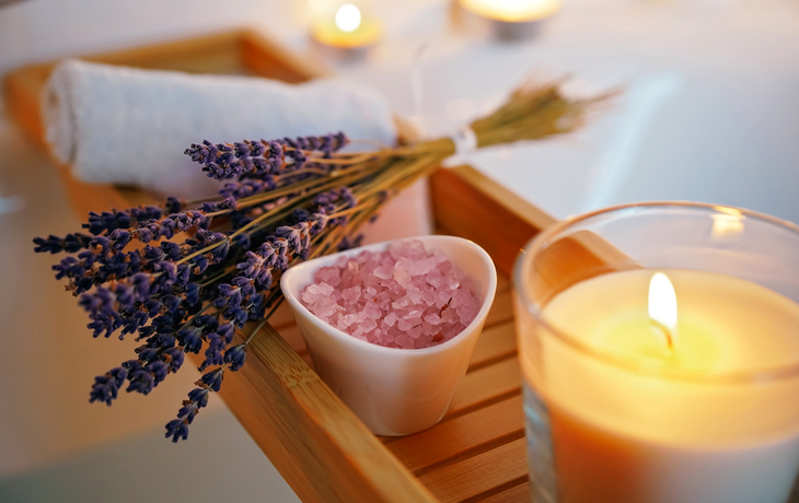 Lavendel, Badesalz, brennende Kerze auf Badewannenablage.