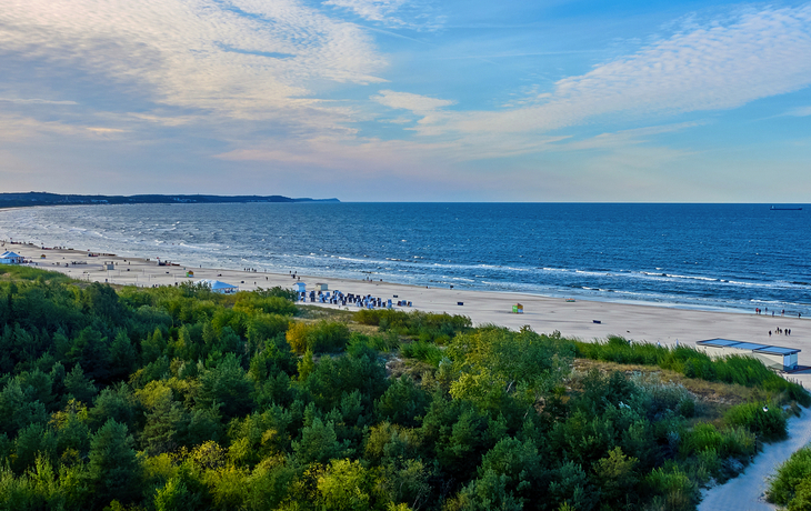 Strandpanorama mit blauem Meer und grüner Vegetation im Vordergrund.